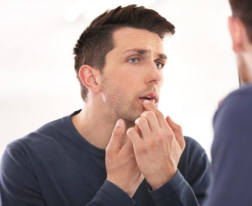 Man examining face in the mirror. touching a cold sore