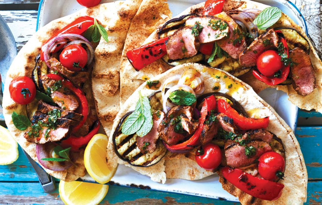 Smoky lamb flatbreads with mint chimichurri Flatbread filled with lamb, red peppers, tomatoes and mint on a blue table