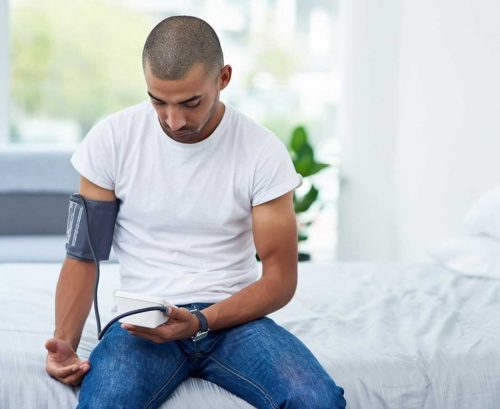 Man sitting on a bed checking his blood pressure