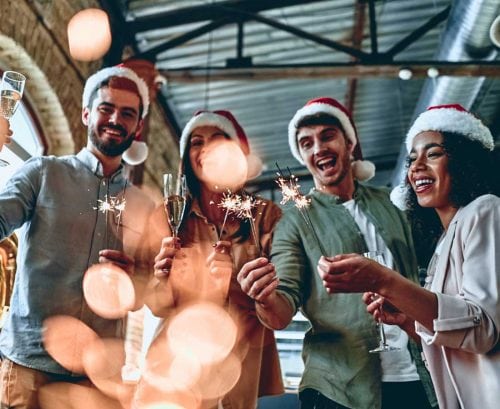 Four people toasting wine with Christmas hats on