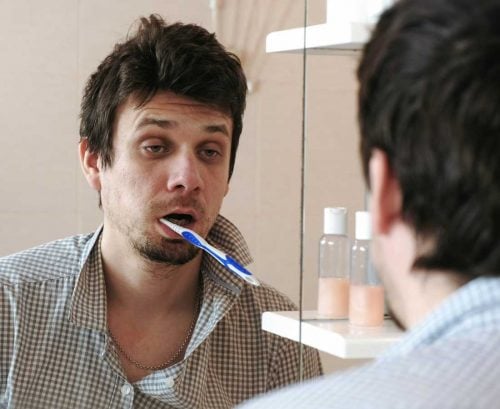 tired man brushing teeth in bathroom mirror