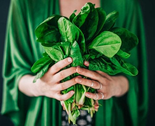 Woman in green holding a bunch of spinach