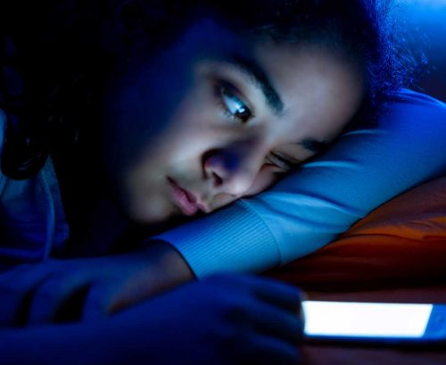 Teenage girl looking at phone screen in bed