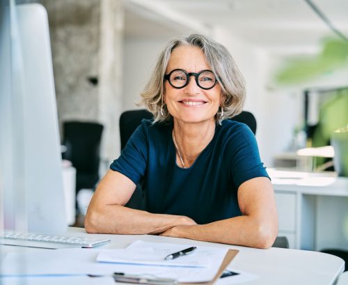 Happy older professional woman wearing glasses smiling from behind her computer