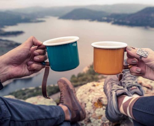 Man and woman drinking tea in front of view from mountain
