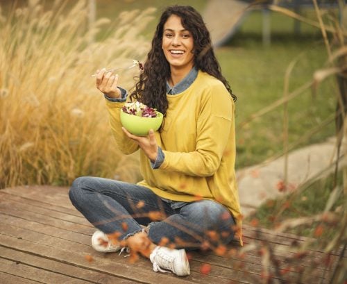 Woman eating a plant-based meal, sitting crossed legged outside