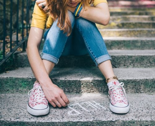 Sad teen girl writing 'help' on pavement