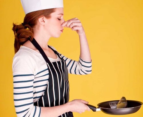 Woman with a fish in a frying pan, holding her nose