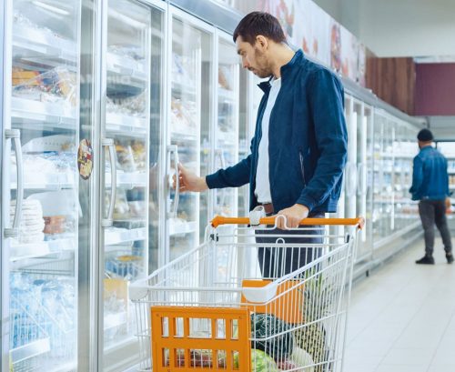 Man choosing frozen meal in supermarket freezer