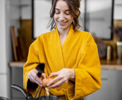 Woman in yellow dressing gown cracking eggs into a pan