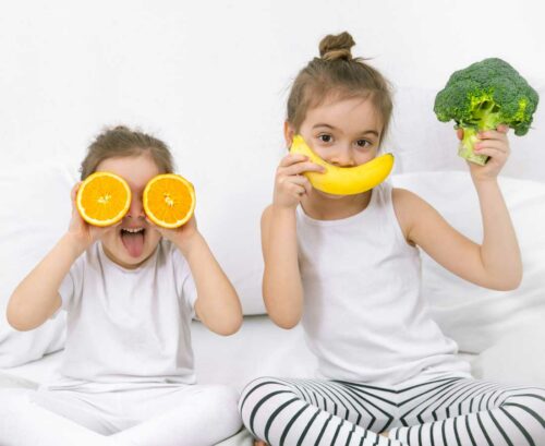 Two girls playing with fruit and vegetables
